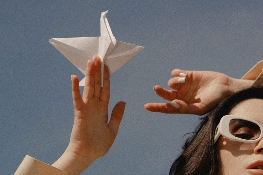 Person holding a white paper crane against a clear blue sky